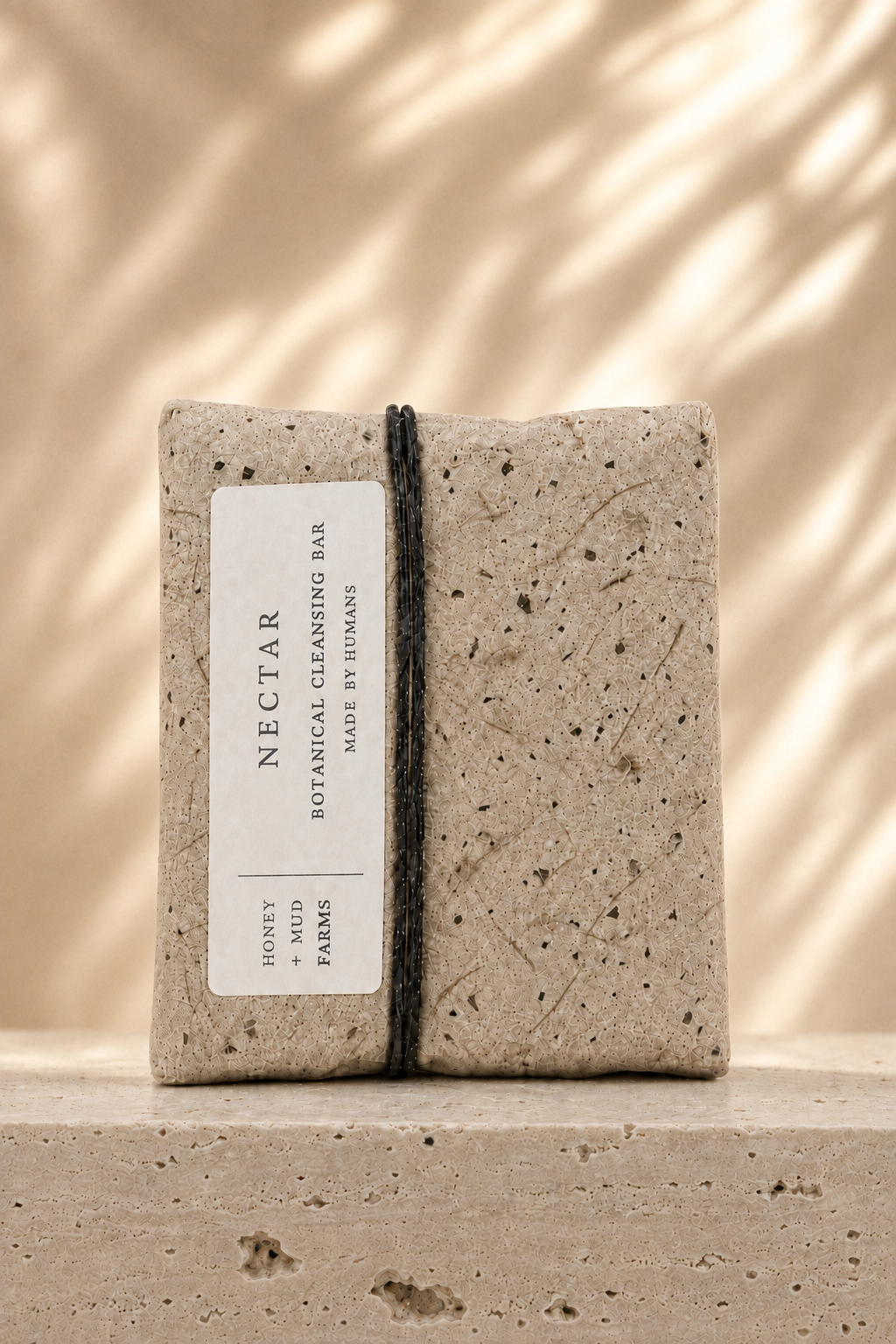 A rectangular bar of NECTAR Botanical Body Bar wrapped in a textured concrete-like sleeve with a white label, standing upright on a matching stone surface against a warm beige background with soft leaf shadows.